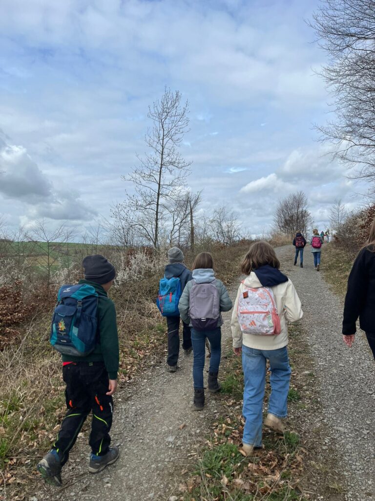 Neun Kinder mit Rucksäcken wandern von hinten den Hügel hinauf.
